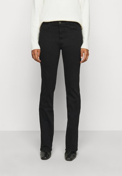 Schwarze gerade Jeans mit glatter Textur, Knopfverschluss und Fünf-Taschen-Design. Kombiniert mit einem cremefarbenen Pullover und schwarzen Schuhen.