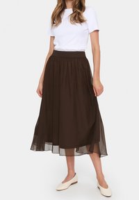 Gonna marrone di lunghezza midi realizzata in materiale leggero e trasparente con una cintura elastica; abbinata a una maglia liscia e tinta unita.