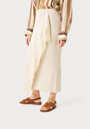 Falda midi beige acanalada con borde de flecos, combinada con sandalias planas de ante marrón y una camiseta de manga larga a rayas.