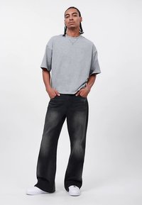 Camiseta cinzenta de manga curta com corte descontraído, combinada com jeans pretos de perna larga com ligeiro desbotamento. Ténis brancos completam o visual.