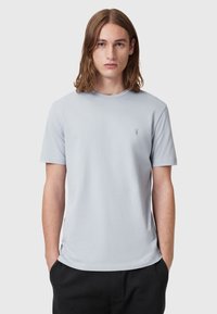 Jasnoszara koszulka z krótkim rękawem wykonana z bawełny, z okrągłym dekoltem i małym logo na lewej piersi. Gładka faktura.