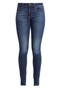 Jeans ajustados de mezclilla azul oscuro. Presentan un clásico diseño de cinco bolsillos, cremallera frontal con cierre de botón y un ligero desgastado en los muslos.