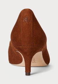 Barna velúr magassarkú cipő, hegyes orral és karcsú sarokkal. Varrott részletekkel és egy kis logóval a tetején.