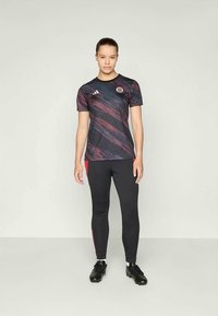 Svart sportskjorte med rød og lilla abstrakt mønster, med Adidas-logo. Fitted svarte leggings med røde detaljer på siden.