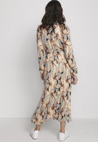 Langärmliges Kleid aus hellgrauem Stoff, mit floralem Muster in Pfirsich- und dunklen Farbtönen, gebundenem Taillengürtel und fließendem Saum.