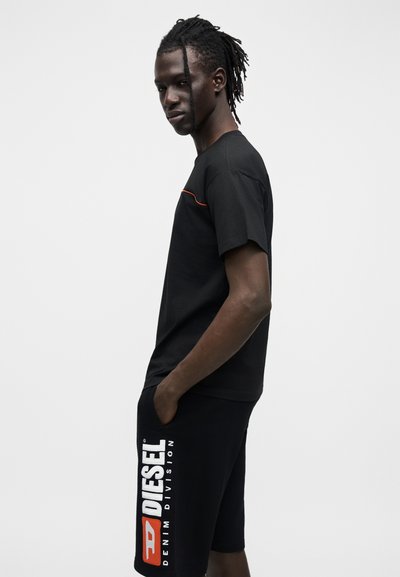 T-shirt en coton noir à manches courtes avec un accent orange. Associé à un short noir avec le logo "DIESEL" en blanc et rouge. Texture lisse.