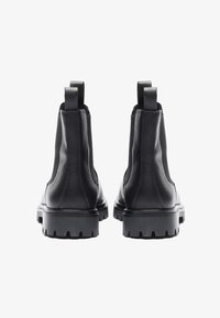 Sorte læder ankelstøvler med en tekstureret overflade, elastiske sidepaneler og en robust gummisål. Har trækflapper for nem påtagning.