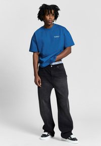 Blue cotton t-shirt with short sleeves and logo, paired with black wide-leg jeans and black sneakers with white accents.