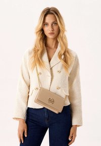 Béžový tvídový blejzer s dvojitým zapínaním, zlatými gombíkmi a zodpovedajúcou béžovou crossbody taškou. Model má na sebe tmavé džínsy, svetlé pozadie.