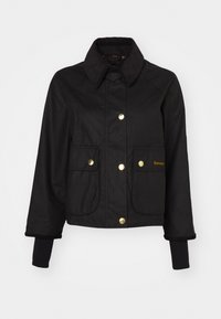 Zwarte cropped jas van stof met een corduroy kraag, gouden drukknoopjes en twee voorzakken. Heeft ribbelgebreide manchetten.