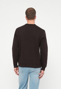 Mørkebrune sweatshirt med ribbet rund hals, lange ermer og rett kant, laget av myk stoff med minimale detaljer. Kombinert med lyse jeans.