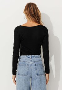 Chemise noire à manches longues avec un décolleté large, associée à un jean en denim bleu clair taille haute avec deux poches arrière.