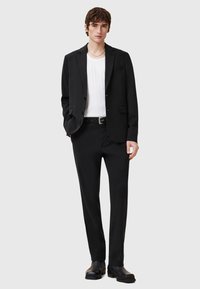 Black suit jacket with two buttons, paired with white ribbed t-shirt and tailored black pants, completed with black ankle boots.