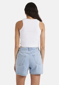 Weißes, geripptes Tanktop, kombiniert mit hellblauen Denim-Shorts mit hoher Taille, geschwungenen Gesäßtaschen und gelben Nähten.