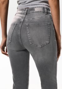 Jean en denim gris au design ajusté, avec deux poches arrière, un léger dégradé et une petite étiquette de marque sur la ceinture.