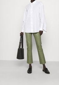 Biała koszula z długim rękawem, zielone dopasowane spodnie, czarne mokasyny i usztywniona czarna torebka z wzorzystym paskiem.