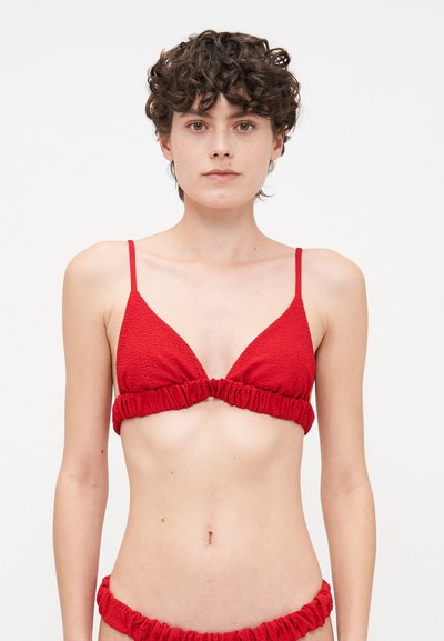 Haut de bikini rouge, avec des bonnets triangulaires en tissu texturé et un bandeau froncé en dessous. Fines bretelles aux épaules. Assorti avec un bas froncé identique.