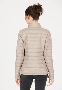 Beige pufferjack met een hoge kraag, een doorgestikt ontwerp en lange mouwen. Gladde textuur met elastische manchetten, gecombineerd met zwarte jeans.