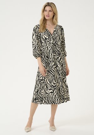 Black and cream striped maxi dress with a wrap design, three-quarter sleeves, soft fabric, and flowing silhouette, paired with light-colored shoes.