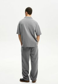 Gray textured short-sleeve shirt and matching relaxed-fit pants, featuring a subtle pattern, with practical side pockets and black footwear.