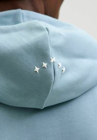 Lichtblauw hoodie met een gestructureerde stof, voorzien van vijf kleine witte steraccenten langs de rand van de capuchon.
