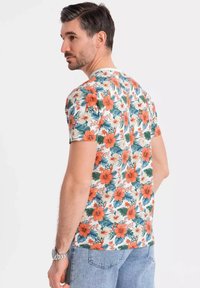 Korte mouwen bloes met een patroon van grote oranje en witte hibiscusbloemen op een crèmekleurige achtergrond, met groene bladeren.