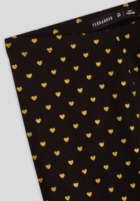 Leggings neri con un motivo completo di piccoli cuori glitterati dorati. La trama del tessuto è liscia, con una cintura elastica per il massimo comfort.