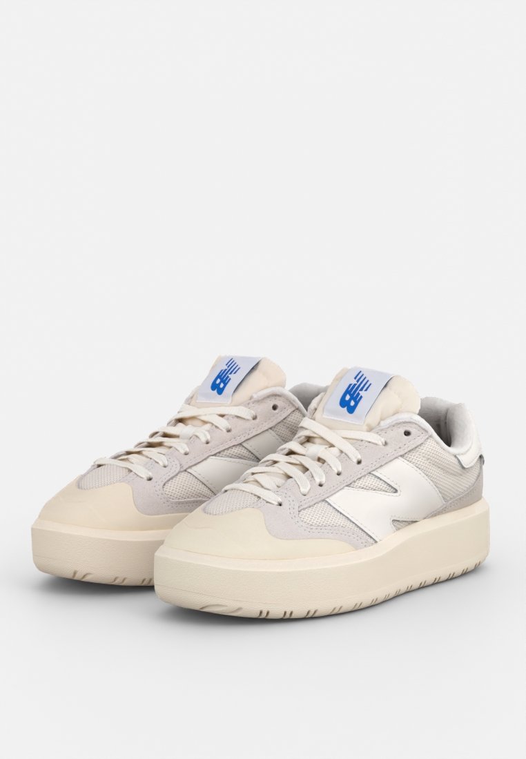 Sneaker mit einer klobigen beigen Sohle, grauem Mesh- und Wildleder-Obermaterial, weißen Akzenten und einem blauen Logoetikett an der Zunge.