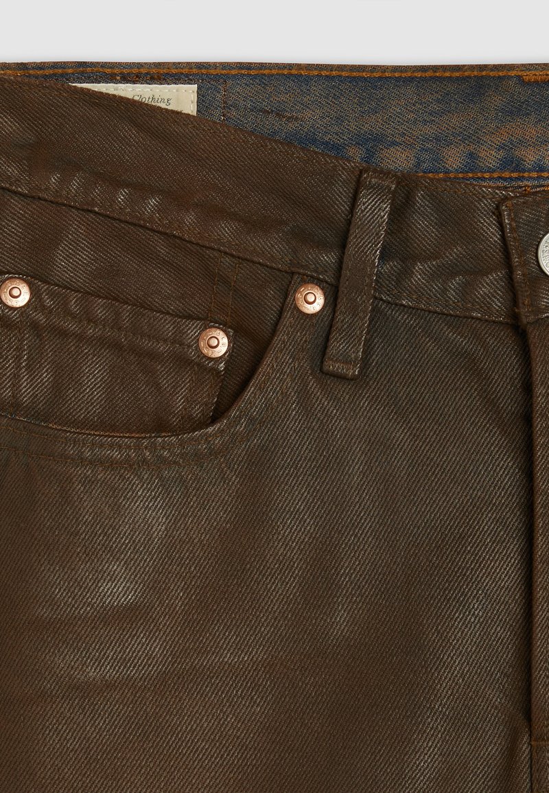 Brązowe dżinsy denimu mają gładką fakturę, prosty krój, miedziane akcesoria i klasyczny pięciopocketowy design.