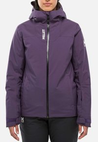 Person wearing a purple hooded winter jacket with front zipper and black pants, standing against a plain white background.