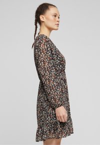 Black floral dress with long sleeves, ruffled hem, and a lightweight, sheer fabric. Features multicolored small flower patterns throughout.