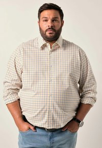Camicia a quadretti gialla e blu; maniche lunghe arrotolate; abbinata a jeans azzurri; orologio nero al polso.