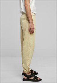 Lys gule joggebukser med teksturert overflate, elastisk midje, sidelommer og baklommer, kombinert med svarte sandaler med stropper.