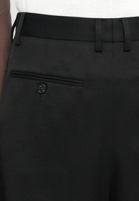 Pantaloni negri cu un material texturat, croi slim, bucle pentru curea și un buzunar posterior cu închidere prin buton.