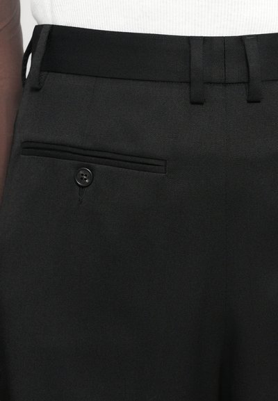 Black trousers featuring a textured fabric, slim fit, belt loops, and a back pocket with a button closure.