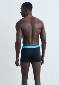 Schwarze Boxer-Briefs mit einem hellblauen elastischen Bund, der das Nike-Logo zeigt, von hinten betrachtet. Glatte Stoffqualität und körpernahe Passform.
