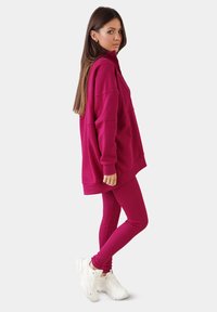 Sudadera fucsia con cuello alto y mangas largas, combinada con leggings a juego, complementada con zapatillas deportivas blancas.