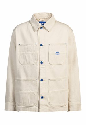 Beige utility jacket with two front pockets, blue stitching, and blue buttons. Made from durable fabric, features a collar and button closure.