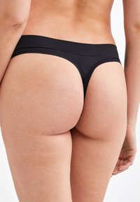 String noir avec une texture lisse, une couverture minimale, une ceinture large et des détails arrière arrondis.