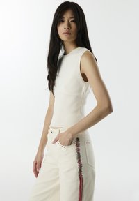 Creme mouwloze ribgebreide top gecombineerd met high-waisted off-white broeken met kleurrijke borduursels langs de zijnaad.