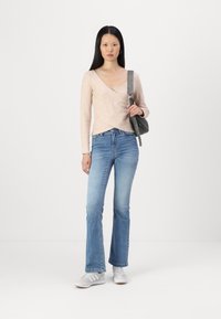 Helles rosa Wickeloberteil, blaue Schlagjeans und graue Umhängetasche. Weiße Sportschuhe mit grauen Streifen. Glatte, weiche Texturen.