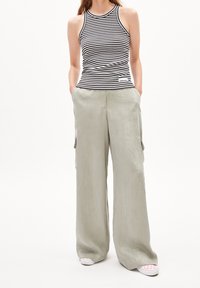 Top a righe bianco e nero con design aderente, abbinato a pantaloni larghi di colore verde chiaro con tasche laterali.