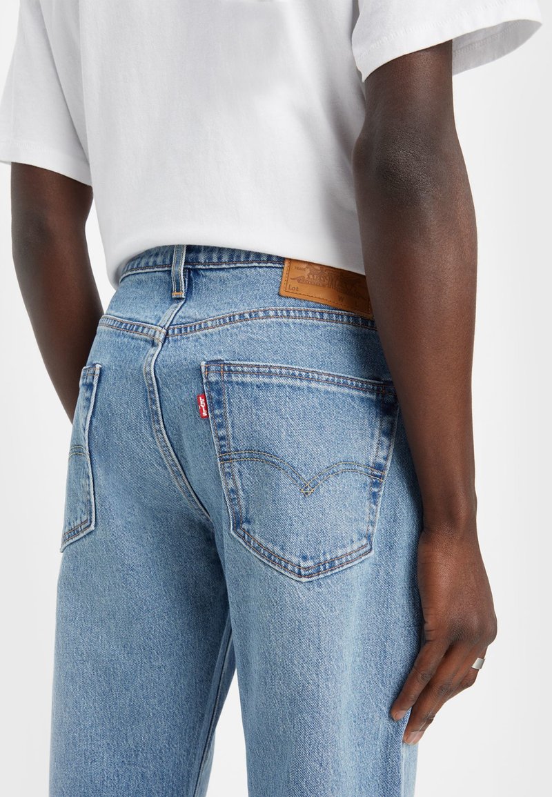 Helle blaue Denim-Jeans mit hoher Taille, versehen mit einem braunen Lederpatch auf der Rückseite und klassischem Steppnähte detail an den Hintertaschen.