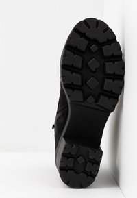 Černá semišová bota s odolnou gumovou podešví, která má hluboké drážky, boční zip a minimalistický design.