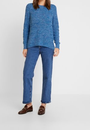 Blauer gestrickter Pullover mit strukturiertem Muster, Rundhalsausschnitt, langen Ärmeln, kombiniert mit blauen Jeans im geraden Schnitt und braunen Slippern.