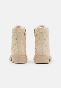 Botines de tobillo de imitación de cuero acolchados en color beige, con tachuelas doradas y forro suave. Cuentan con una suela plana y una lengüeta en la parte trasera para poner y quitar fácilmente.