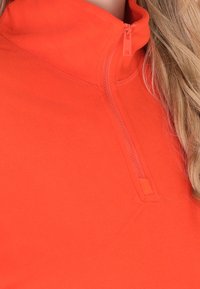 Rode fleece trui met hoge kraag en een ritssluiting aan de voorkant, met een gladde textuur en een getailleerd ontwerp. Geen patronen of accenten zichtbaar.