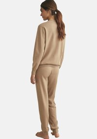 Ensemble de loungewear en tricot beige avec un col rond côtelé, des manches longues et un pantalon fuselé avec des poignets élastiques, vu de dos.