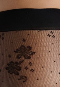 Collant neri a fantasia floreale con finitura trasparente e testurizzata e una vita nera uniforme. Presenta delicati disegni e accenti sparsi.