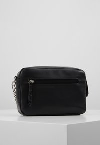 Borsa a tracolla nera in pelle con forma rettangolare, tasca frontale con zip e tracolla a catena. Texture liscia e design minimalista.